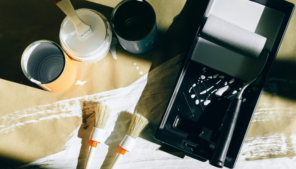 Top view of painting tools including brushes, rollers, and paint cans on paper.